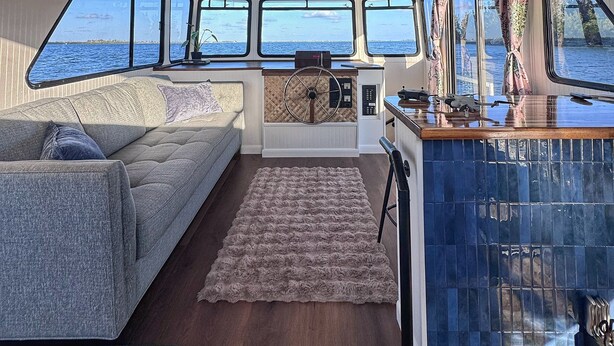 Interno di un'imbarcazione con divano, tappeto, timone e vista sul mare.
