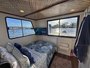 A cabin with a bed, a window with a view of the water, a mounted TV, and a fire extinguisher.