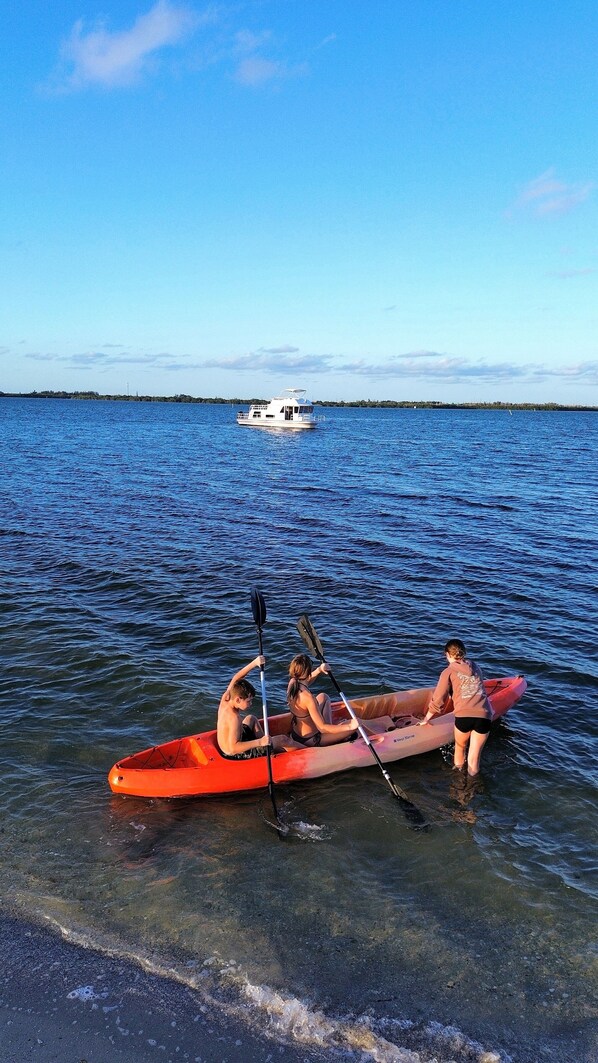 Un kayak sobre aguas tranquilas, con un barco a la distancia y un cielo despejado.