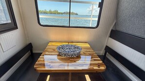 Ambiente interno compatto con tavolo, due panche e una finestra vista sull'acqua.