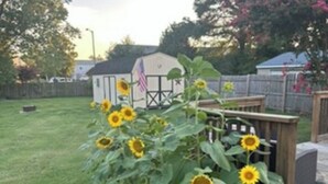 Ein Garten mit Sonnenblumen, einer Holzdielenveranda und einem kleinen Gartenhaus mit einer amerikanischen Flagge.