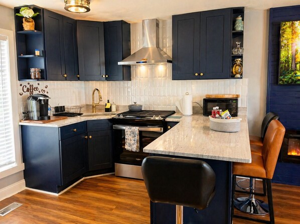 A modern kitchen with dark cabinetry, a central island, a stove, and a bar area.