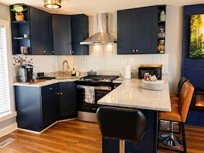 A modern kitchen with dark cabinetry, a central island, a stove, and a bar area. - Modern Cozy Retreat Near Starved Rock w/ King Bed (Ottawa)