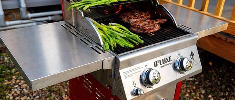 Una parrilla portátil con base roja y parte superior de acero inoxidable, que cuenta con un sistema de doble energía y un panel de control.