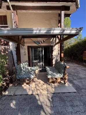 Ein überdachter Patio-Bereich mit zwei Sitzgruppen, einem Deckenventilator und Blick ins Haus.