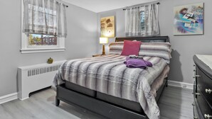A bedroom with a bed, a radiator, a lamp, and artwork on the wall.