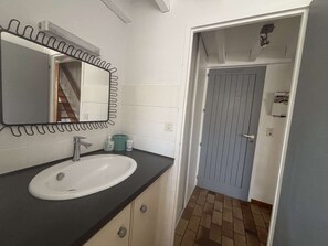 A bathroom with a white sink, a mirror with a black frame, and a door leading to another room. - Vacances proches du lac ! (BISCARROSSE)