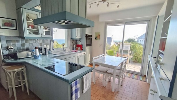 Una cocina con una isla central, una mesa de comedor y vistas a través de un ventanal.