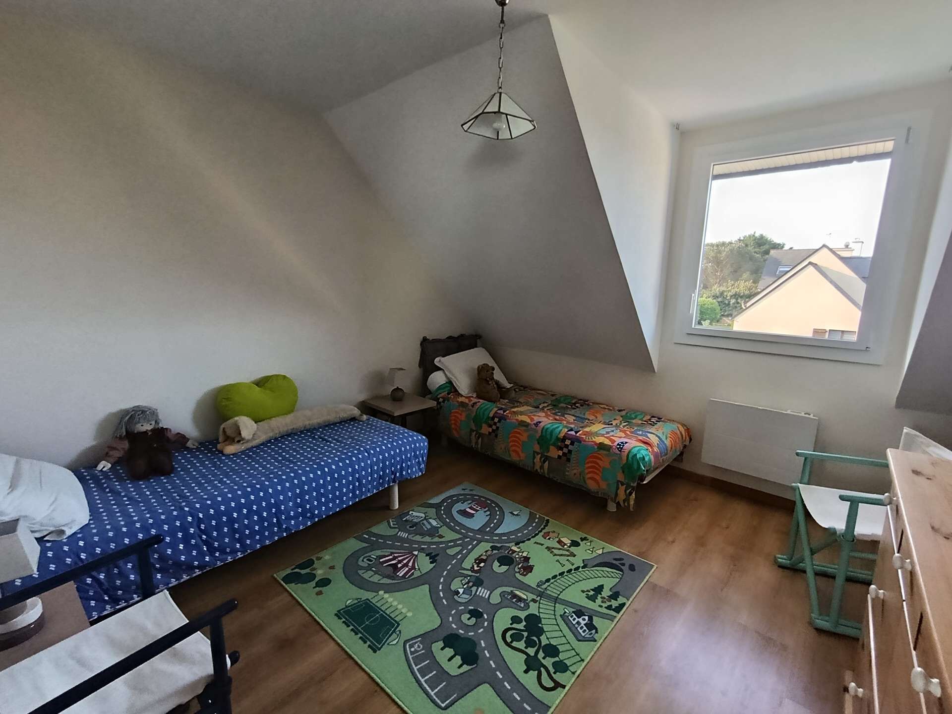 Ein Schlafzimmer mit zwei Betten, einem Fenster, einer Hängelampe und einem Teppich.