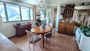 Un comedor con una mesa y sillas de madera, un candelabro, una cocina al fondo y una escalera que sube.
