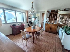 Ein Essbereich mit Holztisch und Stühlen, einer Chandelierleuchtre, einer Küche im Hintergrund und einer Treppe, die nach oben führt.