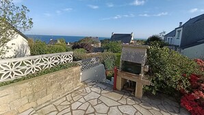 Un patio de piedra con una valla blanca decorativa, una pequeña construcción de piedra y vistas al mar.