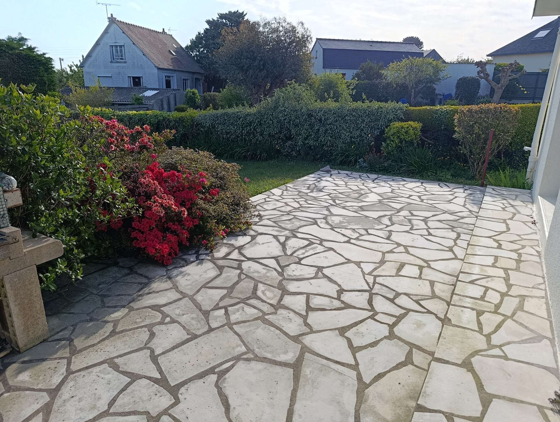 Een terras van natuursteen dat leidt naar een huis met tuin en hagen.