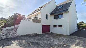 Une maison moderne à deux étages, dotée d’une porte de garage rouge, d’un toit en pente et d’une petite fenêtre à l’étage supérieur.