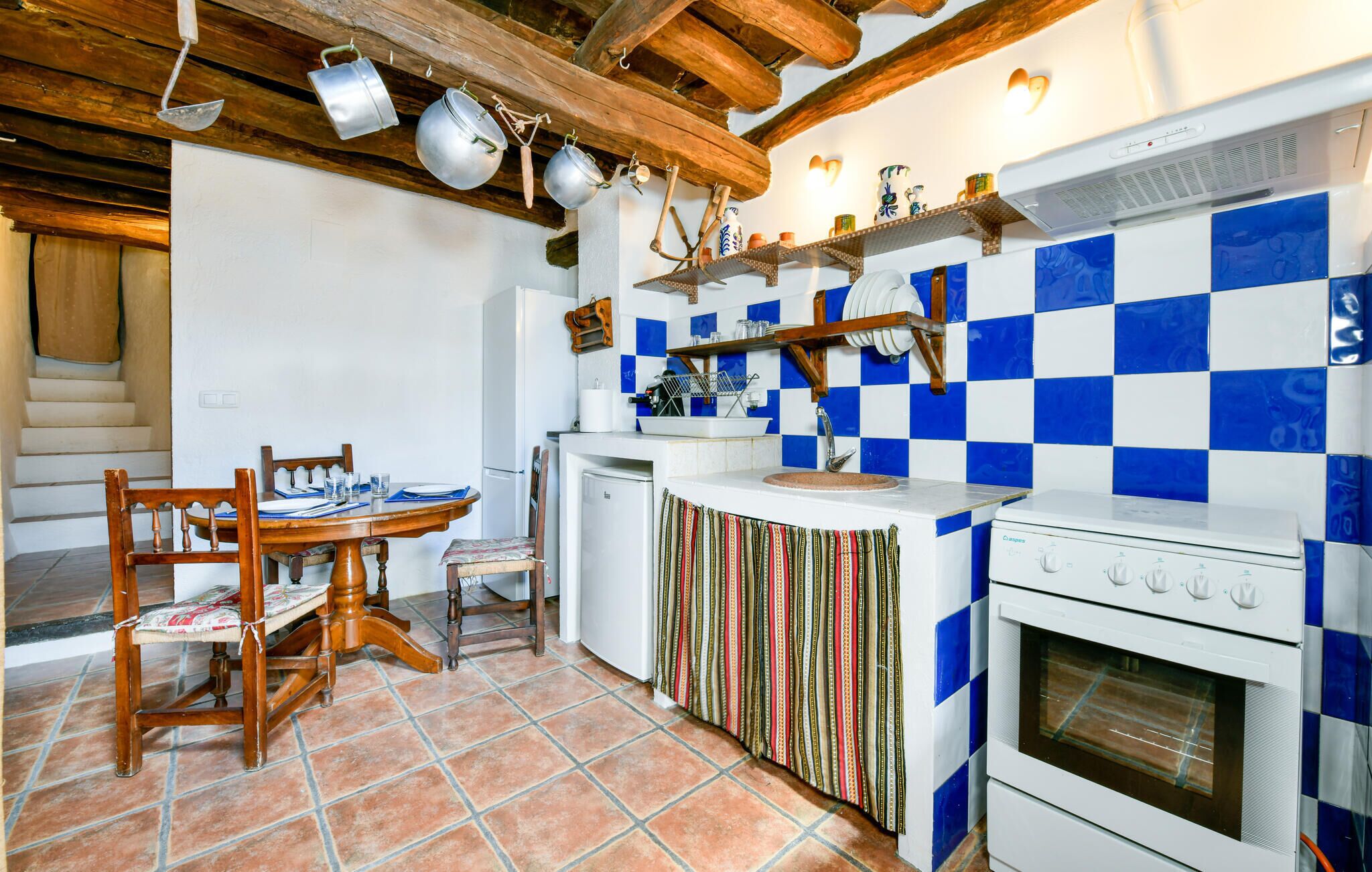 Una cucina con zoccolo a scacchi, travi in legno al soffitto, pentole appese e un fornello.
