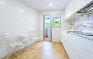 A compact kitchen with a dining area, wooden flooring, and a view through a glass door.