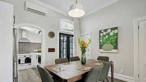 Un comedor con una mesa de madera, sillas tapizadas de verde, un jarrón con flores y un cuadro en la pared.