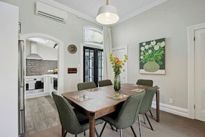 Uma sala de jantar com uma mesa de madeira, cadeiras estofadas verdes, um vaso com flores e um quadro na parede.