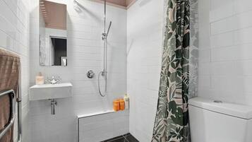 Ein Badezimmer mit weißen Fliesen, einem Waschbecken, einer Dusche und einer Toilette.