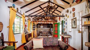 A cozy room with a patterned sofa, wooden beams, a chandelier, and a kitchen area.