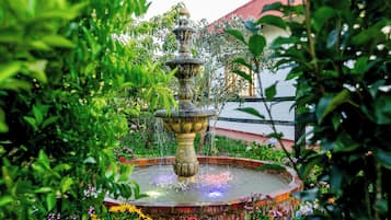 A garden with a central fountain surrounded by lush greenery and flowering plants.