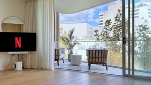 Een moderne woonkamer met een flatscreen-tv, een balkon met uitzicht op gebouwen en bomen, en een schuifdeur van glas.