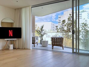 A modern living room with a flat-screen TV, a balcony with a view of buildings and trees, and a sliding glass door. - Executive Designer Stay • Central • Gym • Sauna (Surry Hills)