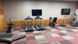 Een sportschool met loopbanden, een elliptische machine, een hometrainer en een bank.