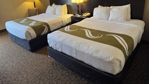 Een hotelkamer met twee bedden, elk met hoofdbord, nachtkastjes met lampen en lijstwerken aan de muren.