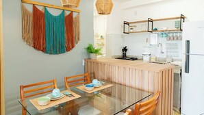 Une cuisine moderne dotée d’un îlot central, de chaises en bois, d’une table à manger en verre et d’une décoration murale en macramé suspendue.