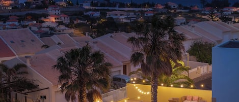 A residential area with houses, palm trees, and a balcony with outdoor furniture.