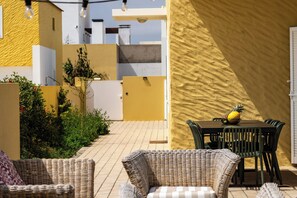 An outdoor patio with wicker furniture, a table with a pineapple, and a yellow textured wall. - Casa da Moagem – Modern and Relaxing Stay (Barroca)