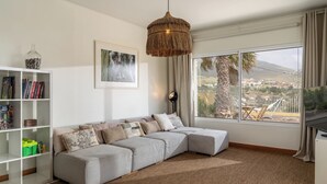 Ein modernes Wohnzimmer mit einem Ecksofa, einem Bücherregal, einem großen Fenster mit Ausblick und einer Pendelleuchte.