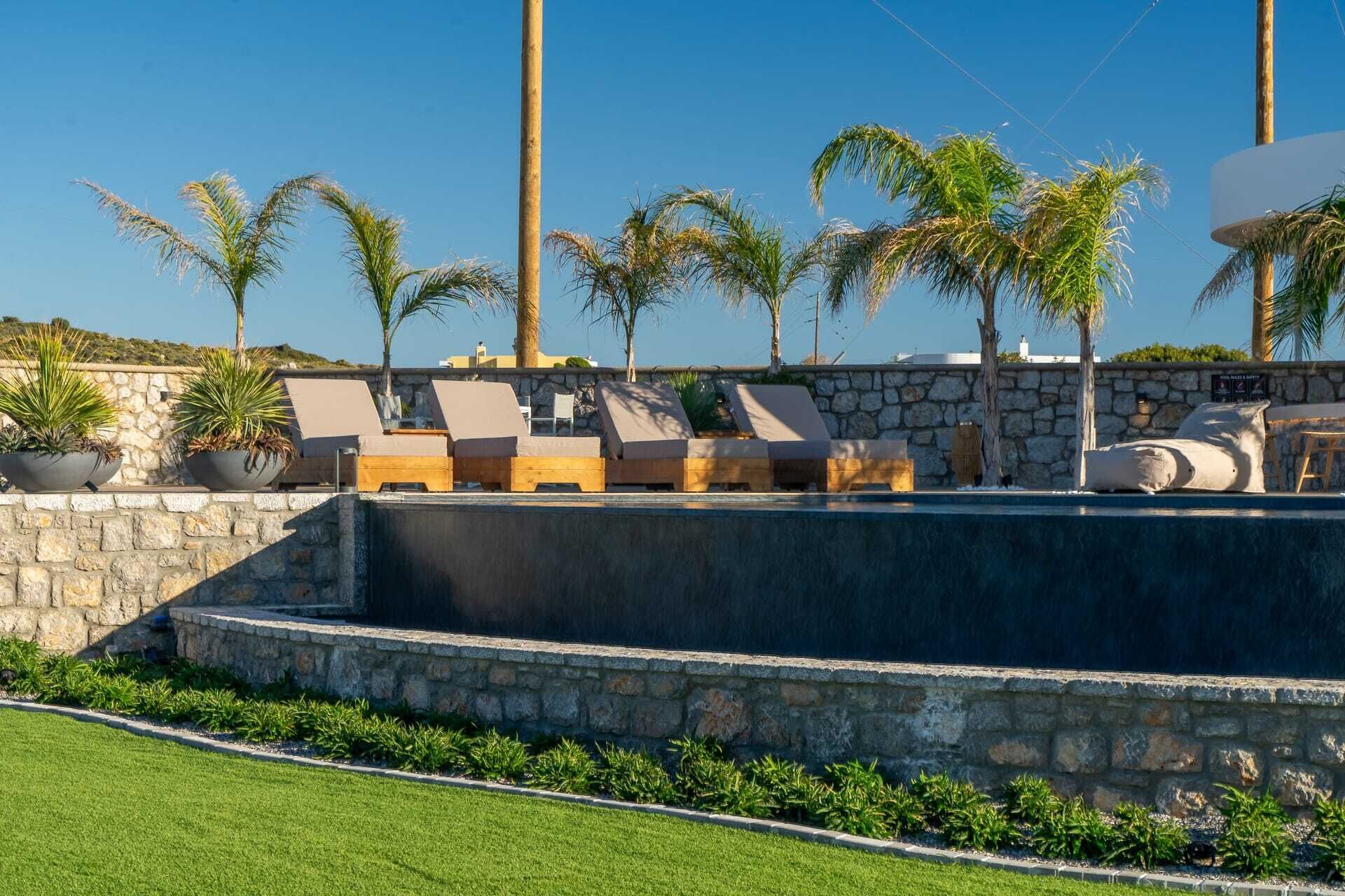 A pool area with lounge chairs, palm trees, and a stone wall.