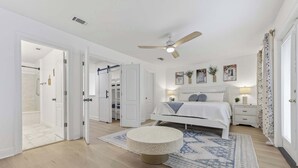 Ein Schlafzimmer mit einem Bett, Nachttischen, einem runden Hocker, einem Deckenventilator und einem gemusterten Teppich.
