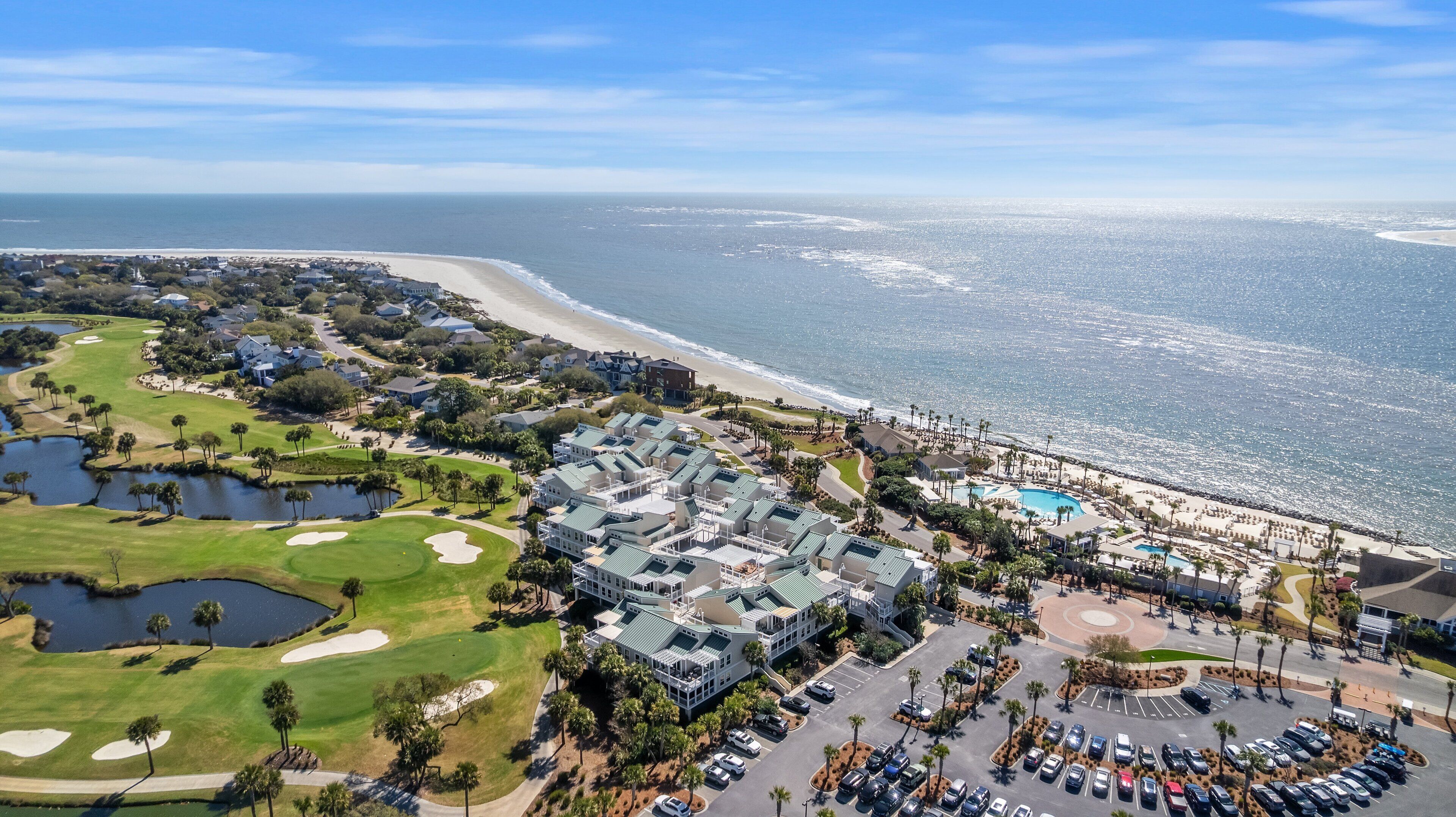 An aerial view of a coastal resort with a golf course, a swimming pool, and beachfront properties.