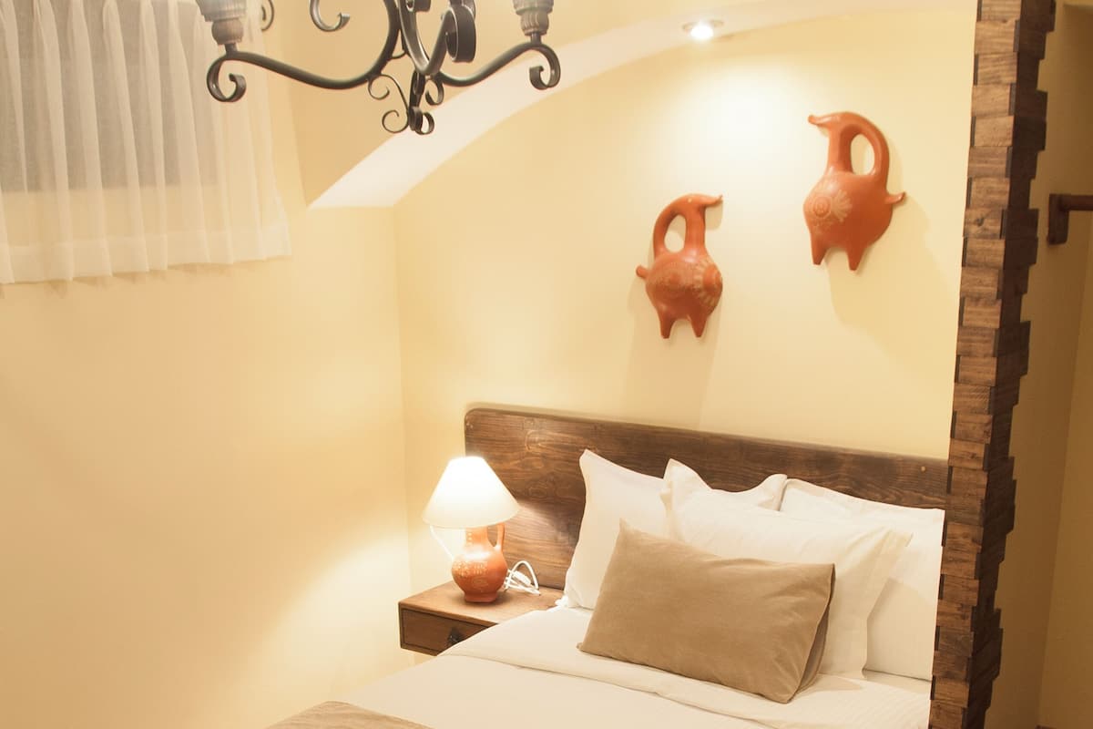 A neatly made bed with a headboard, a bedside lamp, and a wall-mounted light fixture.