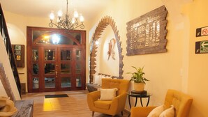 Un vestíbulo con puerta de madera, dos sillones, una mesita con una planta y una araña.