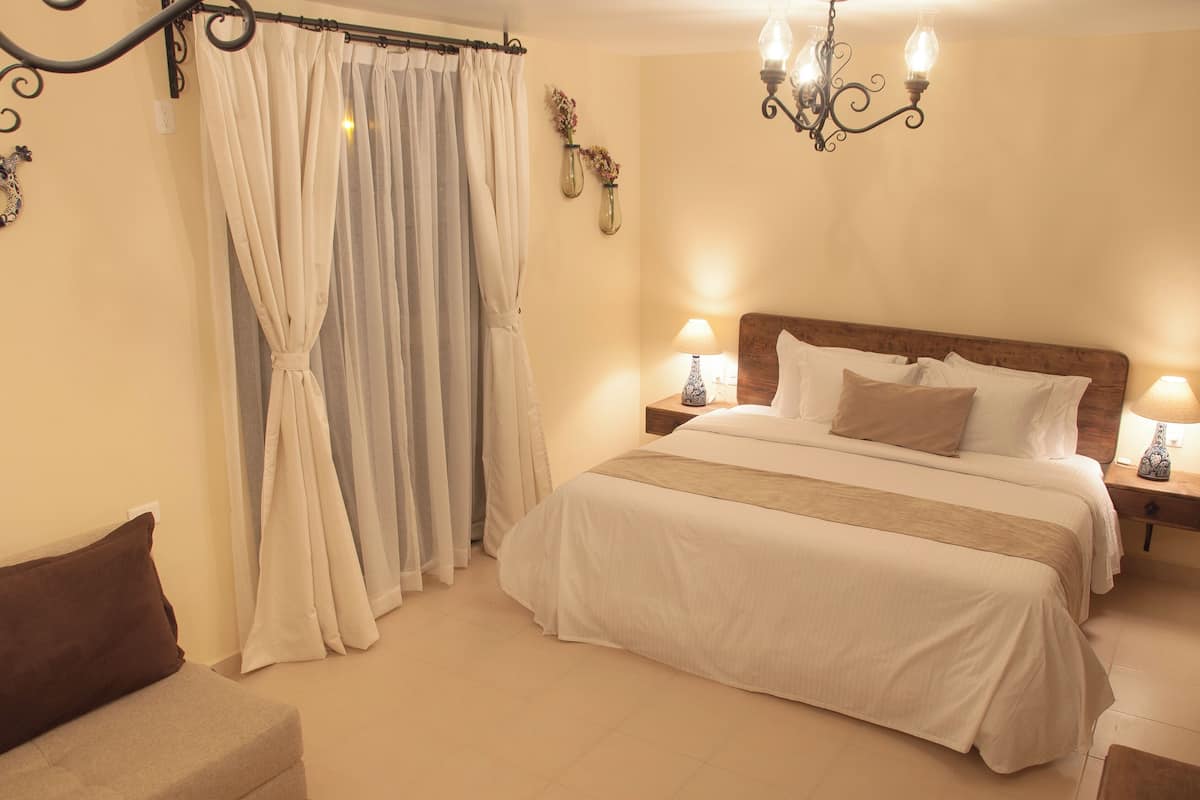 A neatly arranged bedroom with a large bed, two bedside tables with lamps, a chandelier, and a curtain.