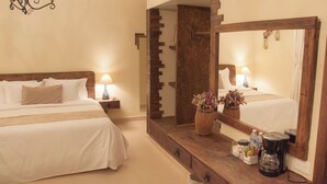 Habitación de hotel con dos camas, un espejo grande, un aparador de madera, una araña y una mesita de noche con lámpara.