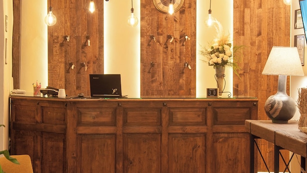 Un mostrador de recepción con una computadora portátil, paneles de madera, lámparas colgantes y un reloj.