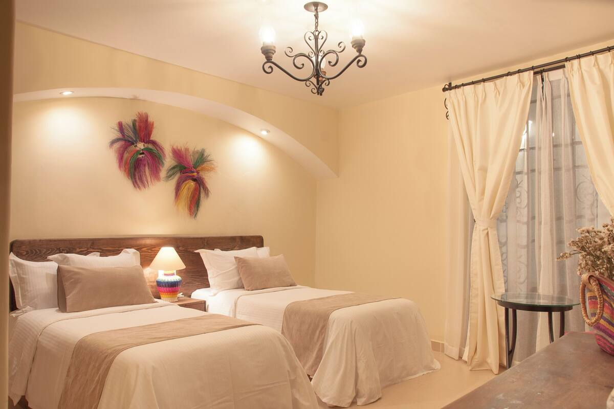 A hotel room with two beds, a chandelier, a small table, and a view of the outdoors.