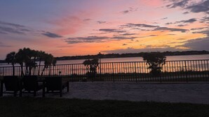 Une vue sur un coucher de soleil au-dessus d’une étendue d’eau, avec une clôture et des bancs au premier plan.