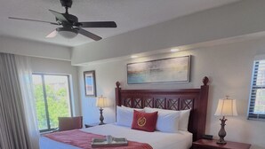 Une chambre d’hôtel équipée d’un lit, d’un bureau, d’une table de chevet, d’un ventilateur de plafond et d’une fenêtre avec des rideaux.