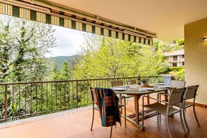 Un balcón con una mesa lista para dos personas, con vistas a una ladera boscosa.