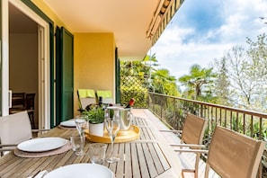 A wooden table set with plates, glasses, and a champagne bottle on a balcony with chairs and a view of greenery.