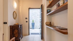 A hallway with a wooden cabinet, a mirror, a shelf with items, and a door leading to a stone wall.
