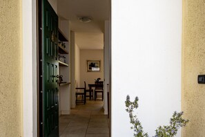 Un couloir mène à une salle à manger où l’on trouve une porte verte, un tableau encadré au mur et une petite plante.