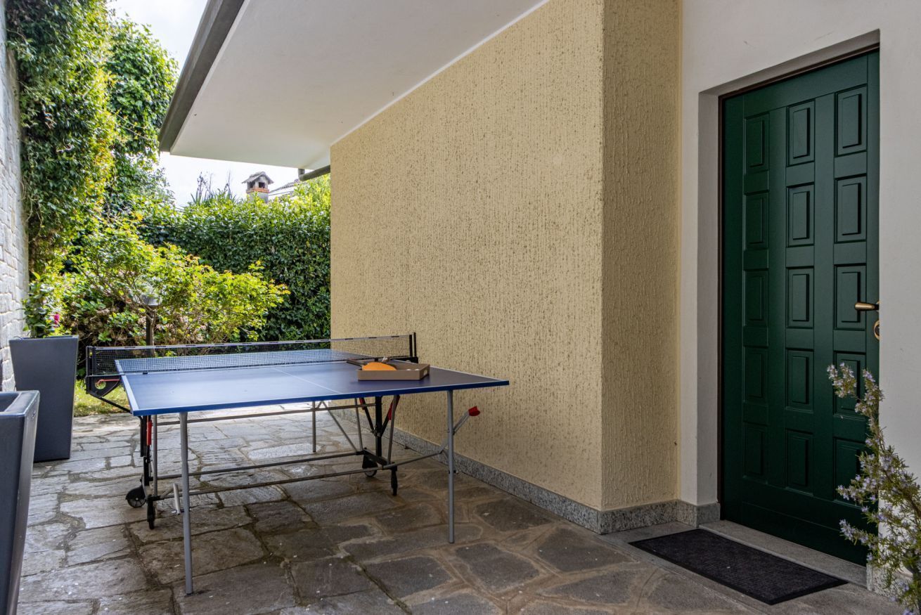 A ping pong table set up outdoors, a green door, and a stone-paved area.
