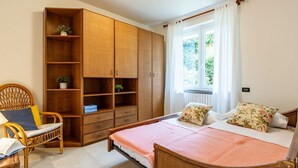 A bedroom with a bed, a wooden wardrobe, a wicker chair, and a window with curtains.